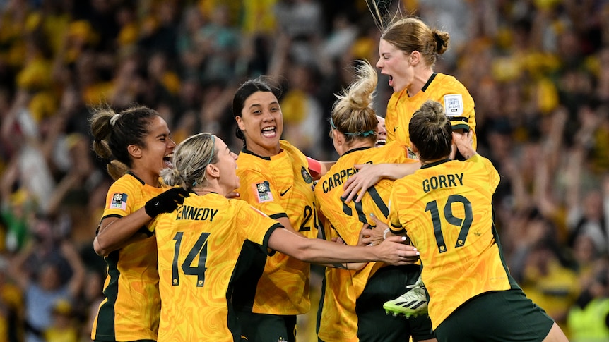 A group pf athletes in yellow shirts celebrate wildly.