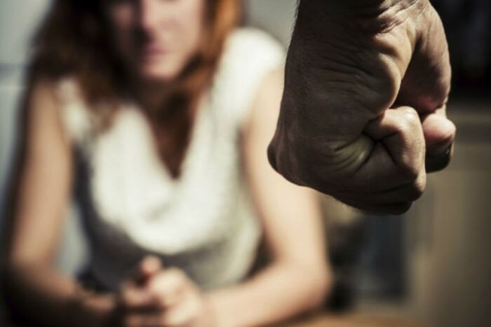 A woman cowers behind a male fist.