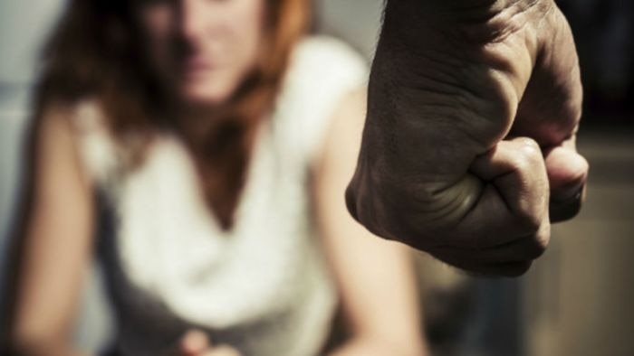 A man's fist is held in aggression in front of a woman in fear 