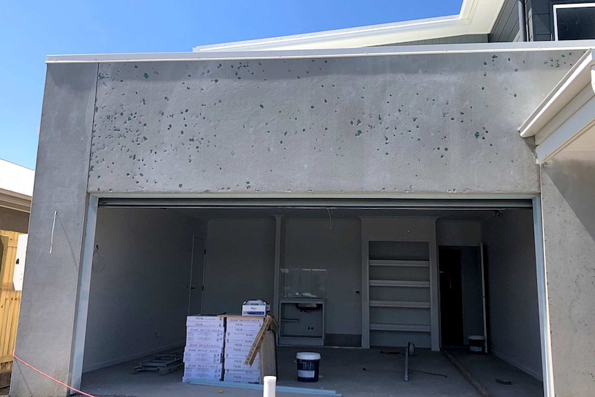 Close up photo of the outside of a house with holes in concrete on one of the walls.