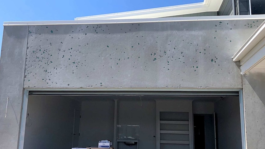 Close up photo of the outside of a house with holes in concrete on one of the walls.