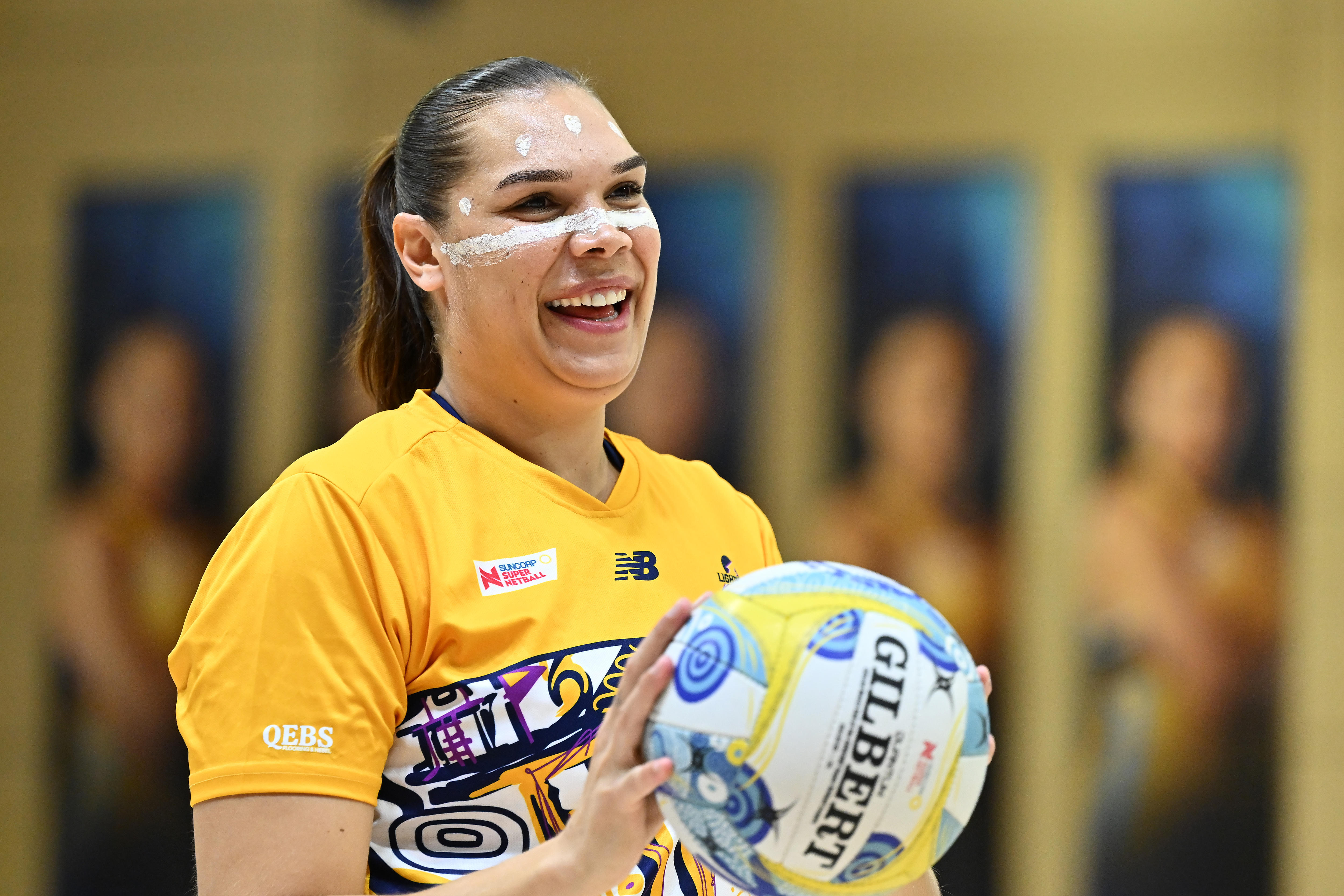 A player holds a netball and has Indigenous paint spotted and striped across her face