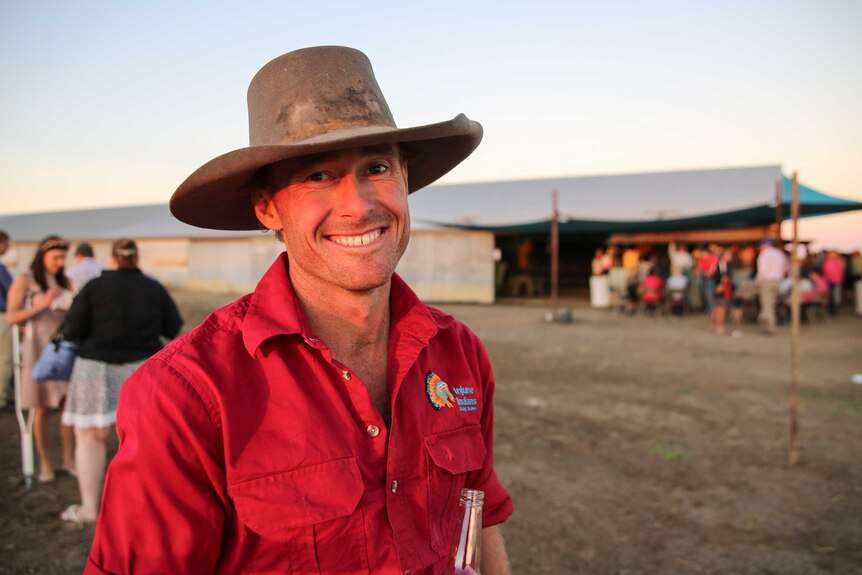 A man wearing a red shirt and brown broad-brimmed hat.