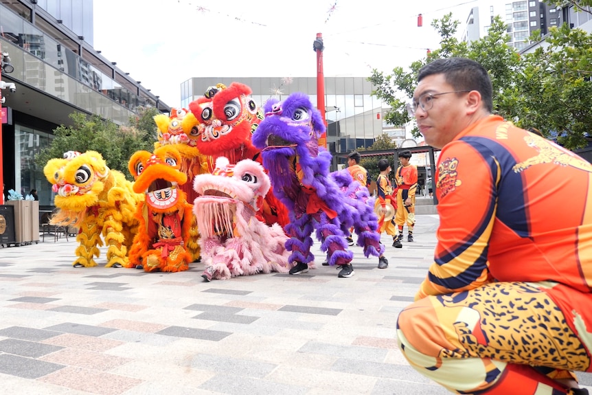 A man squats down in front of a group of six lion dancers