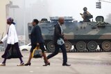 Zimbabwe civilians walk past a tank and a solider