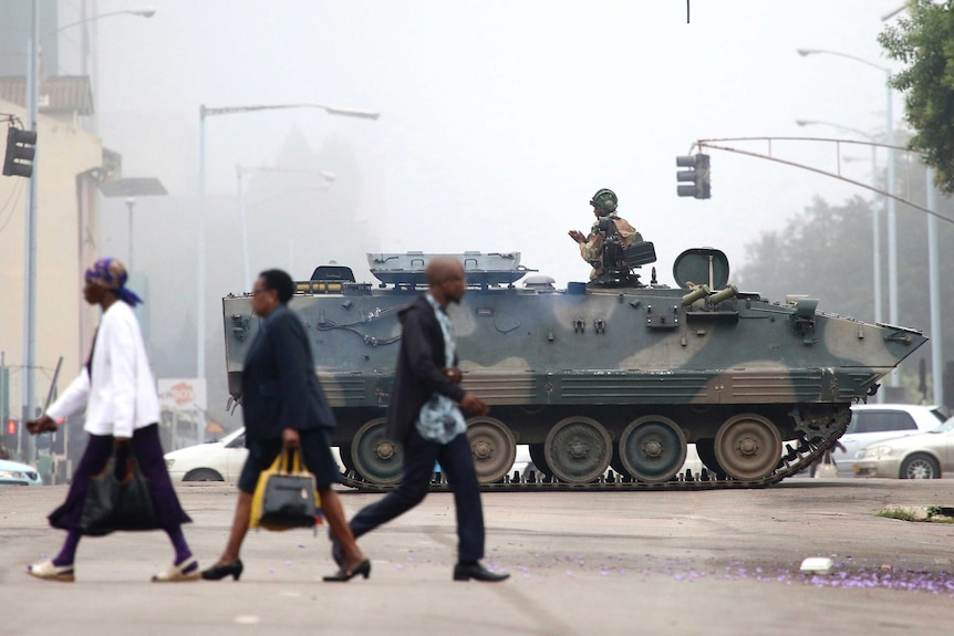 Zimbabwe civilians walk past a tank and a solider