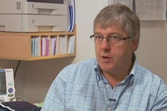 Grey-haired man with glasses, wearing a blue shirt.