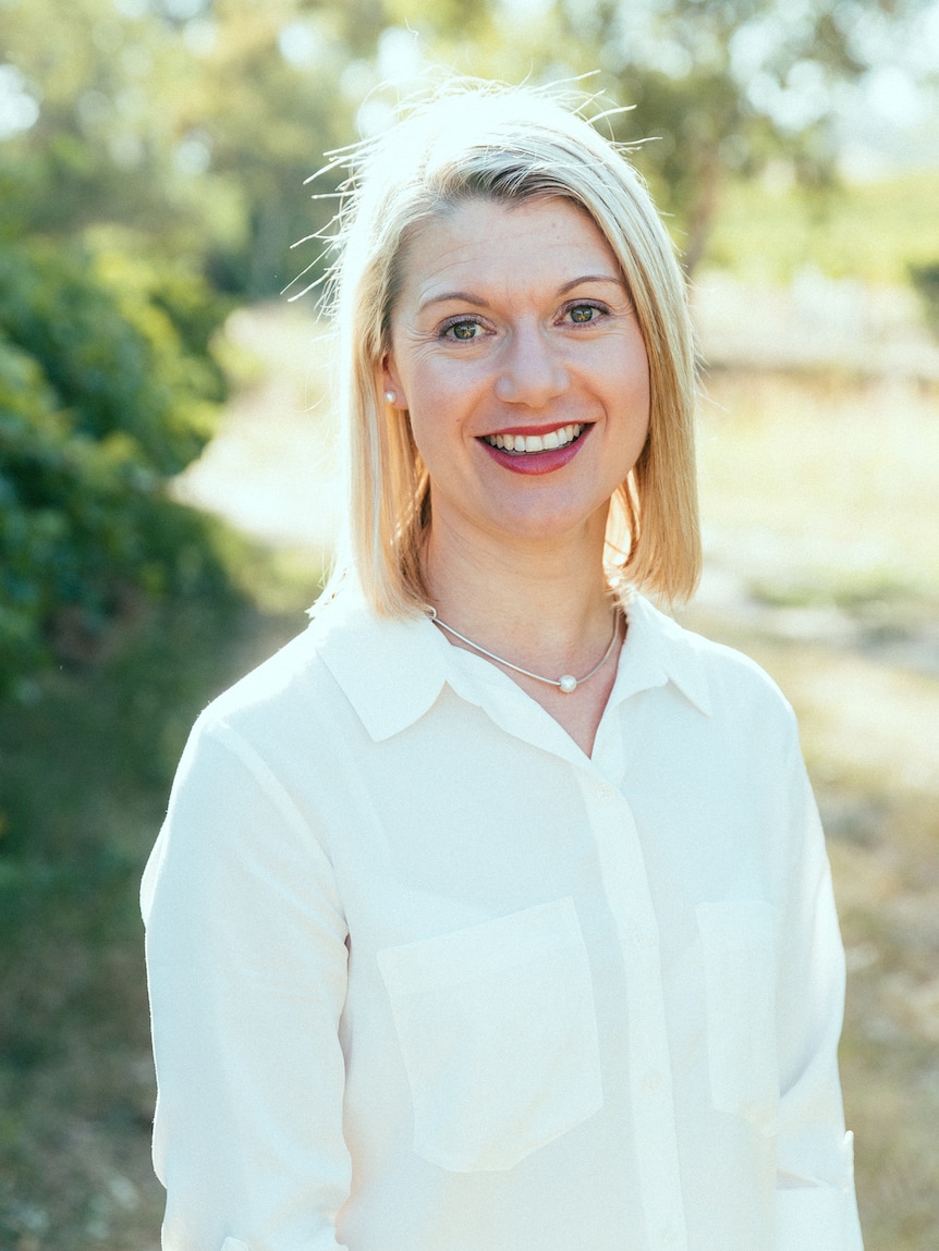 A woman with blond hair wearing a white shirt standing in a vinyard.