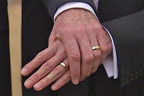 Two men wearing wedding bands holding hands.