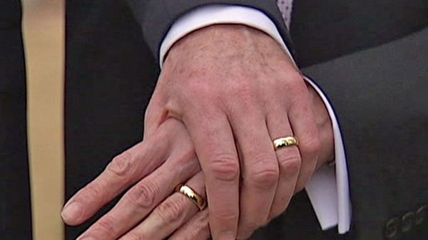 Two men wearing wedding bands holding hands.