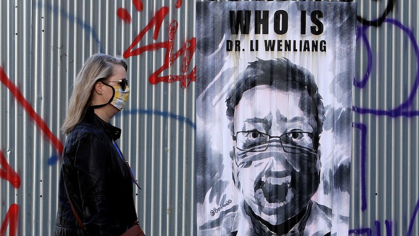 A woman wearing a face mask walks past a poster of late Li Wenliang.