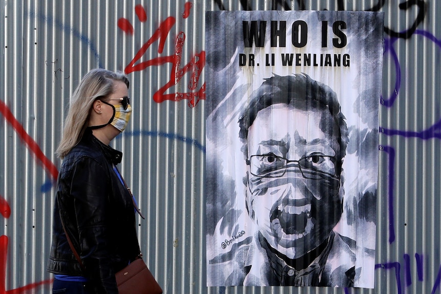 Une femme portant un masque facial passe devant une affiche de feu Li Wenliang.