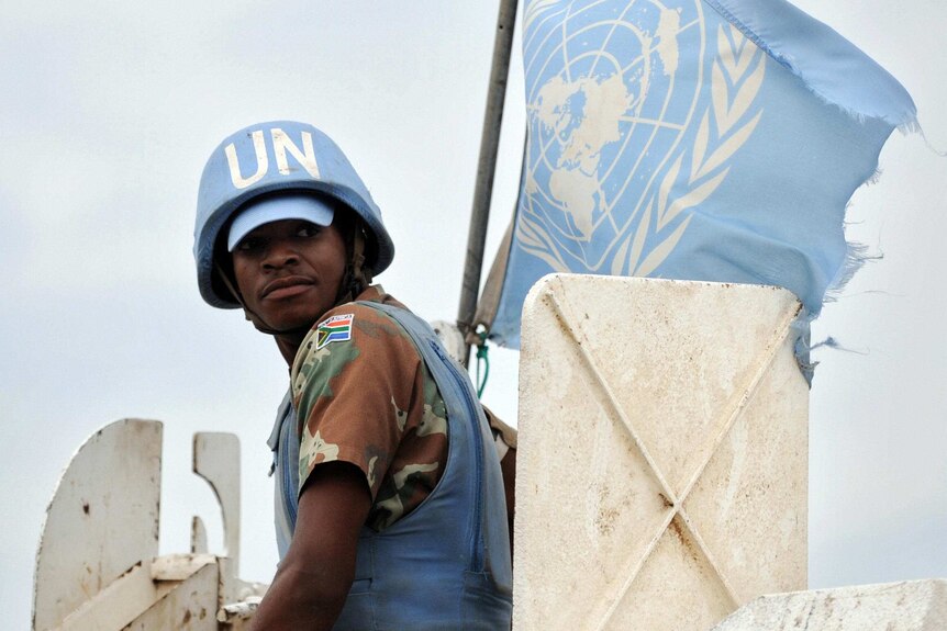 A UN soldier looks over his shoulder. He is on a tank and the UN flag flies