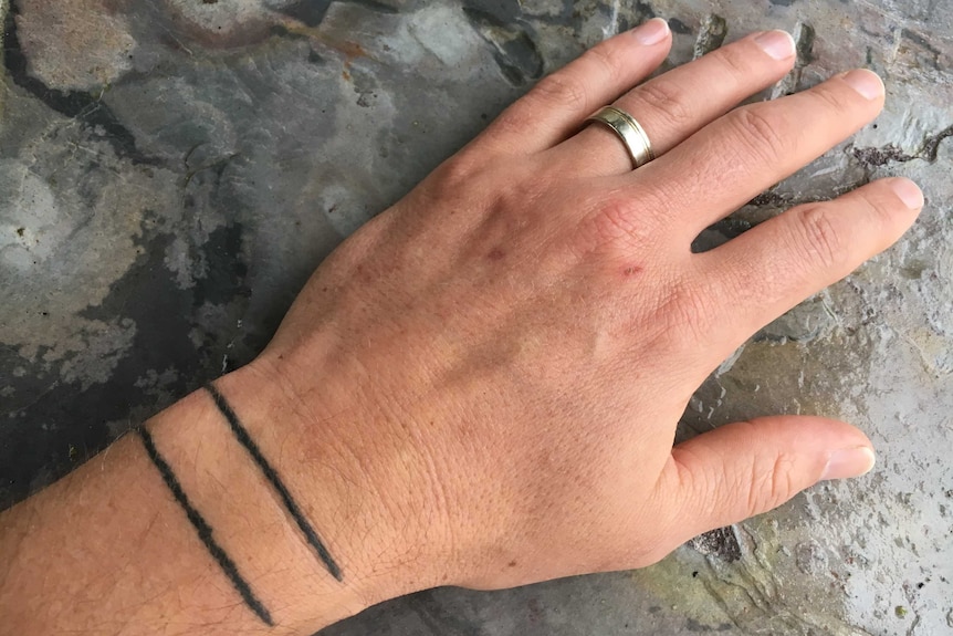 Close-up of a man's hand with two lines tattooed across the wrist.