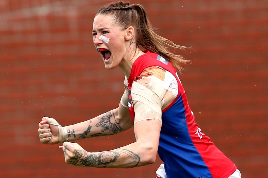 A Melbourne AFLW player pumps her fists as she celebrates kicking a goal in the grand final.