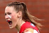 A Melbourne AFLW player pumps her fists as she celebrates kicking a goal in the grand final.