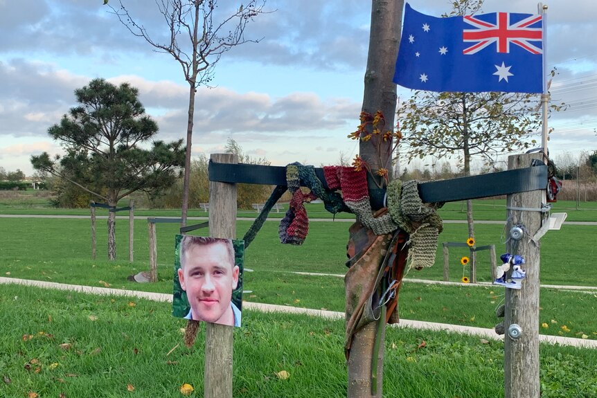 A photo of a man, a scarf and Australia flag are hung from a small tree with lots of lawn around.