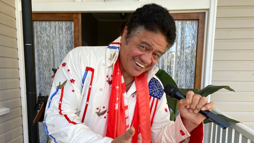 A man dressed in an elvis costume holds a microphone