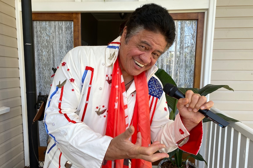 A man dressed in an elvis costume holds a microphone