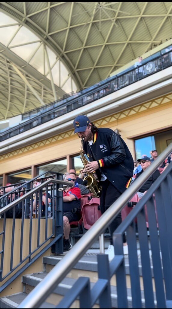 man with baseball hat on plays saxophone in a seated stadium crowd