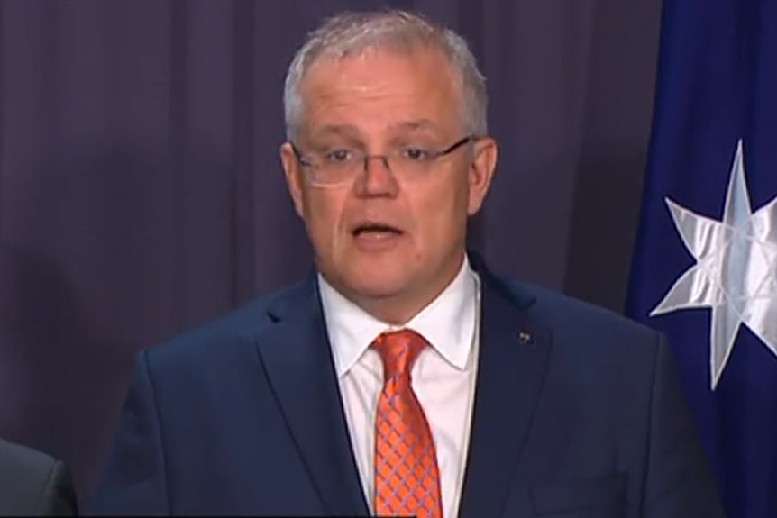 Australian PM Scott Morrison stands in front of the flag, while wearing a blue suit.