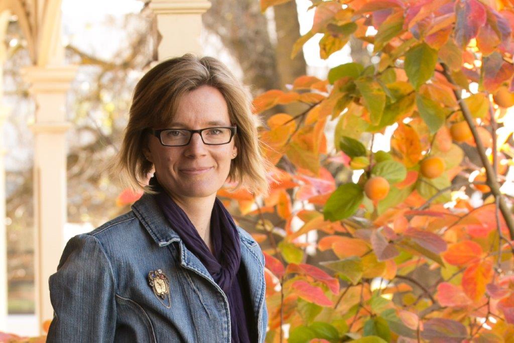 Woman standing in front of a tree with rust-coloured leaves.