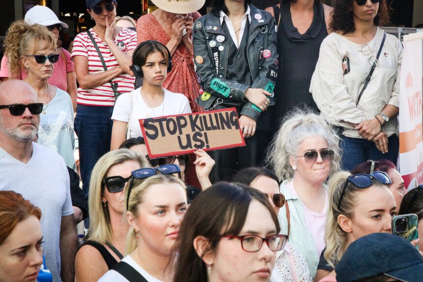 A crowd of people at a rally against gender-related violence holding signs