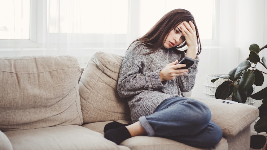 Woman on phone sitting on grey couch looking distressed