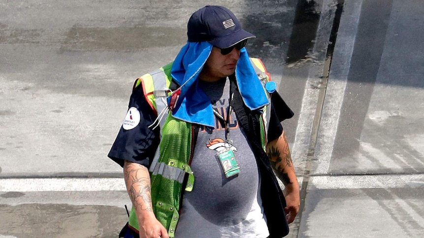 A sweaty ground crew member wears a cap and towel on his head