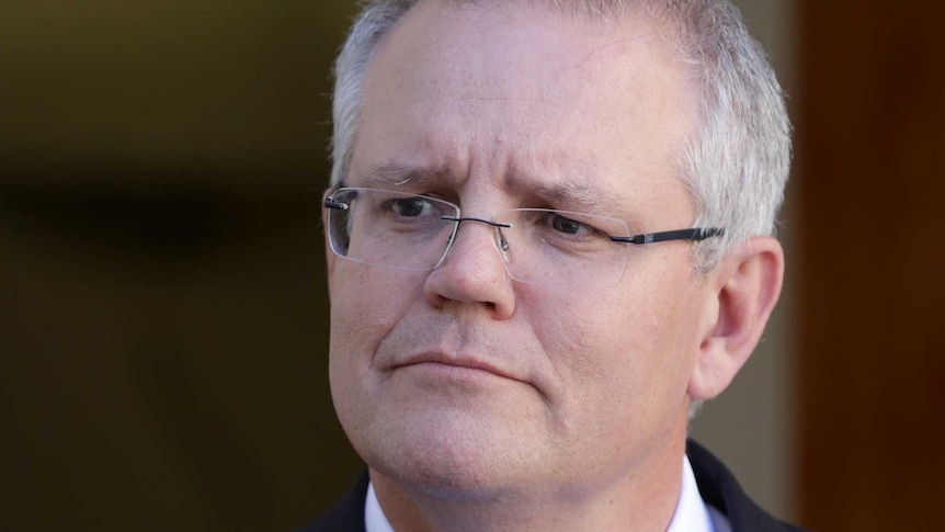 A man with glasses and an Australian flag pin on his jacket looks into the distance