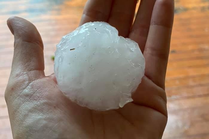 A hand holds a hailstone about the size of a tennis ball.