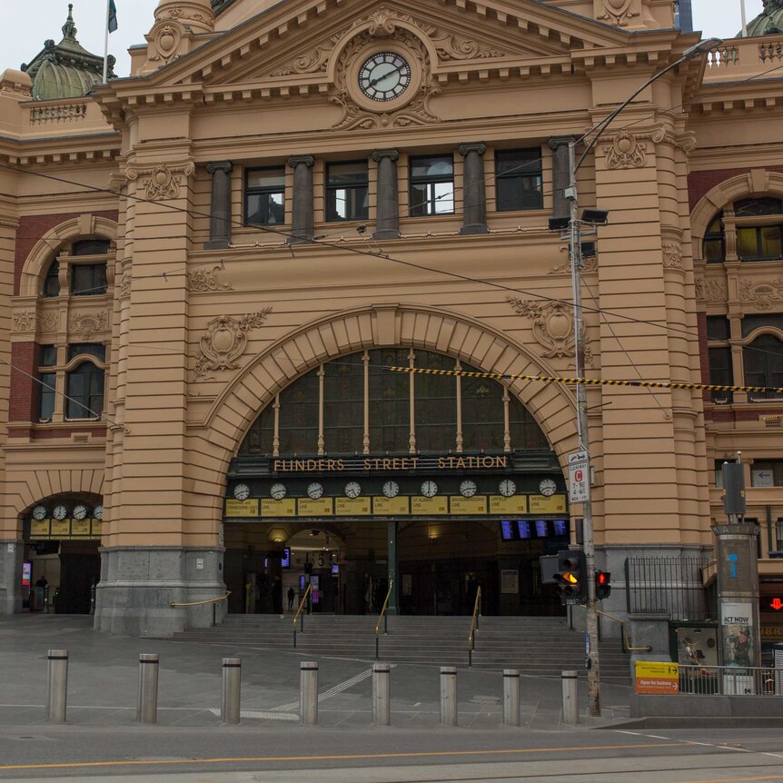 A woman wearing a mask waits to cross a deserted Flinders Street