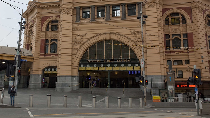 A woman wearing a mask waits to cross a deserted Flinders Street