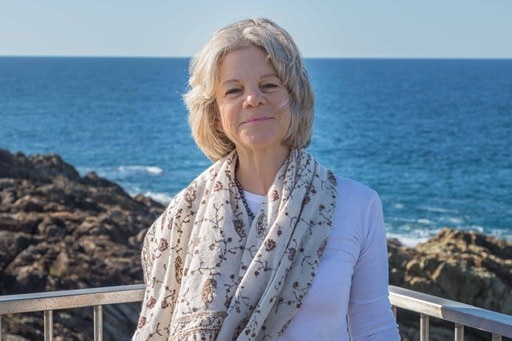 A female in a white shirt and scarf smiling at an ocean lookout.