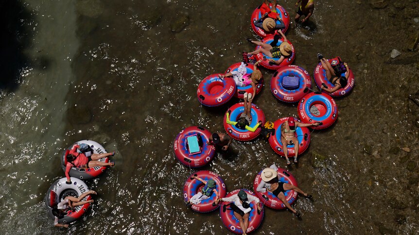people sitting insite red floating tubes on top of the brown water 