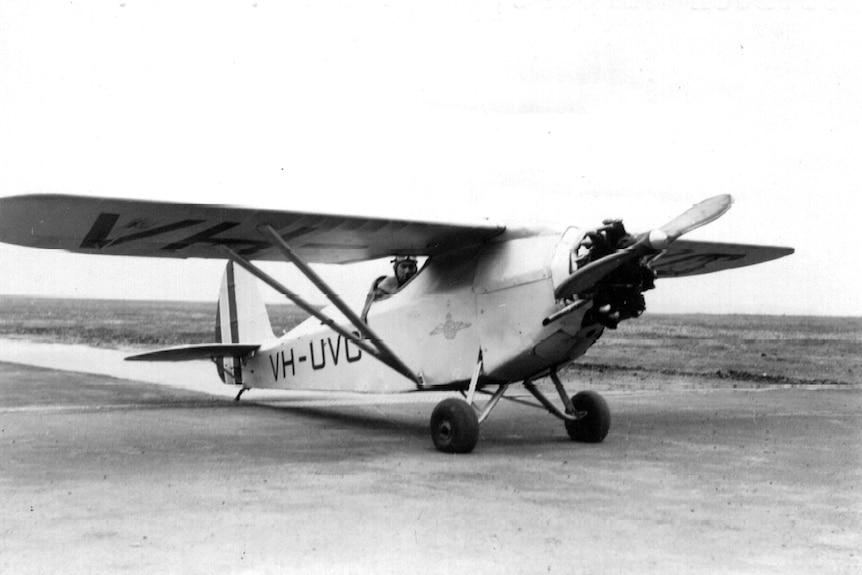 A man with a hat and goggles sitting in the cockpit of Comper VH-UVC Aircraft.