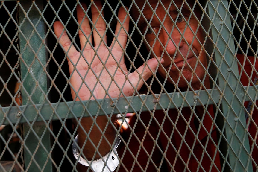 A man puts his hand up to metal mesh bars