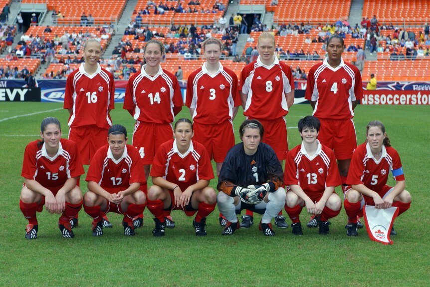 A women's soccer team in red jerseys poses for a photo, in two rows with the front squatting and the back standing.