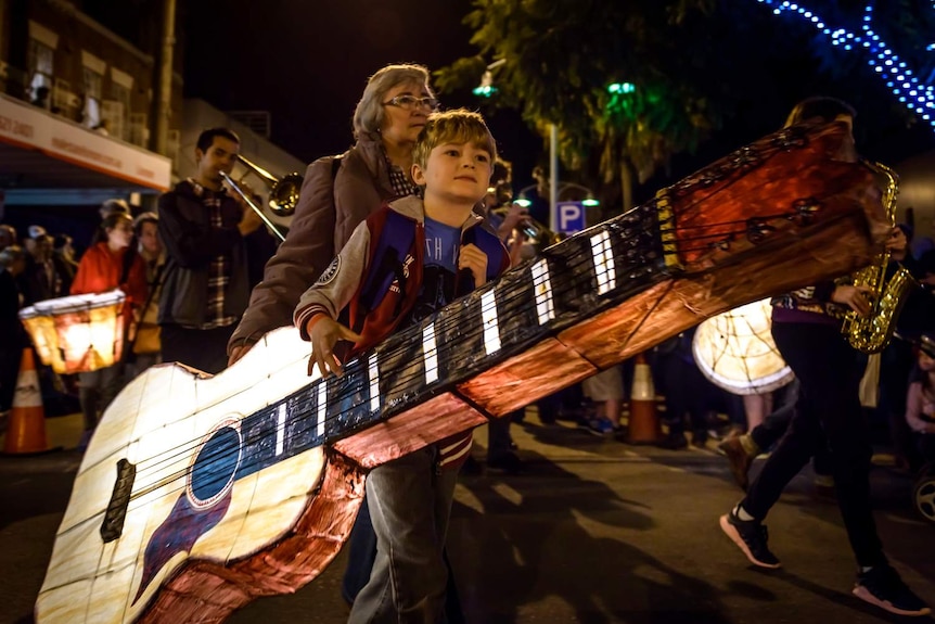 Boy carrying lantern shaped like a guitar.