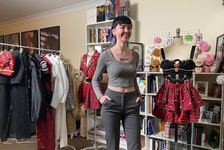 Young woman wearing a grey top and dark jeans stands next to a costume. 