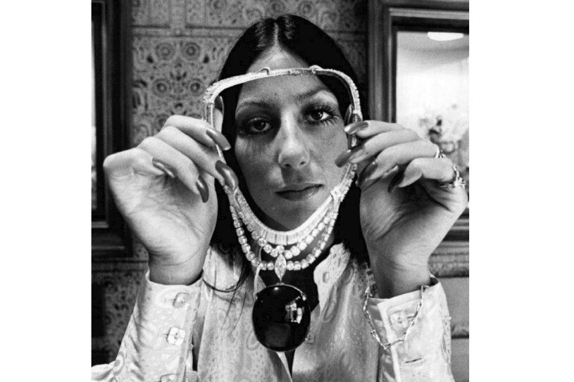 A black and white photo of Cher holding a large sapphire necklace