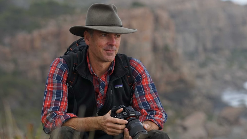 Sean Blocksidge sits on a rock looking out at the Cape Track in the Margaret River, wearing a hat and carrying a backpack.