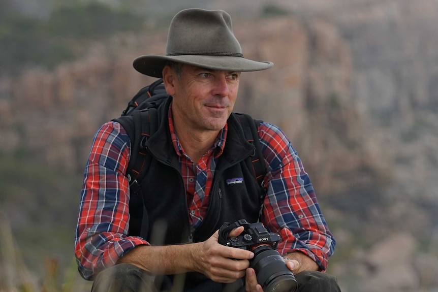 Sean Blocksidge sits on a rock looking out at the Cape Track in the Margaret River, wearing a hat and carrying a backpack.