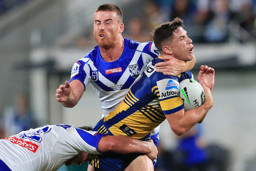 A Parramatta NRL player holds the ball while being tackled around the neck by Canterbury rival.