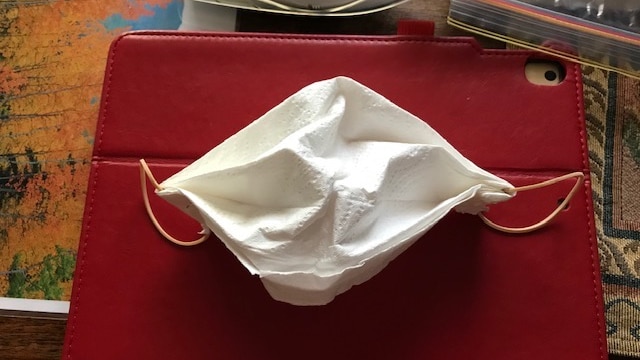 A mask made from paper towel, with a rubber band stapled to it.