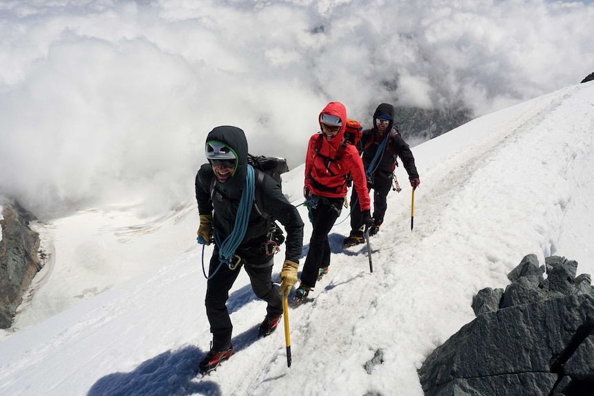 Steve Monks working as a climbing guide in the snow covered Allalinhorn in Switzerland, 4207m, with two other people behind him.