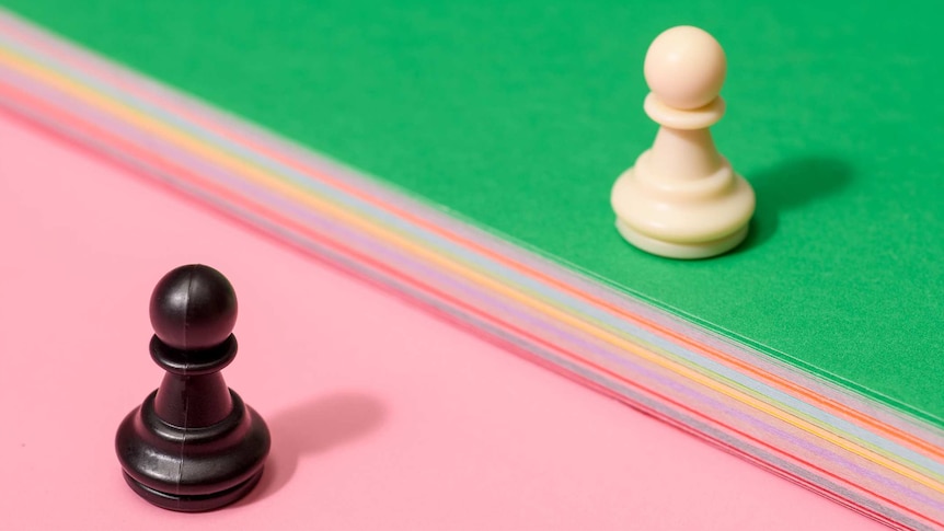 two pawn chess pieces stand on opposing sides divided by multi-coloured cloths running through the middle