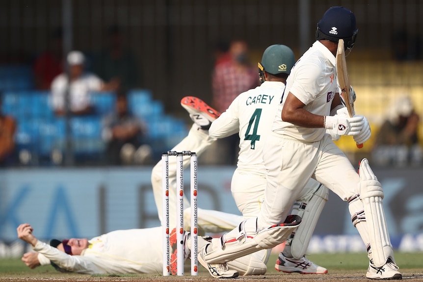 Australia fielder Steve Smith hits the ground after taking a catch to remove India's Cheteshwar Pujara, who's looking back.