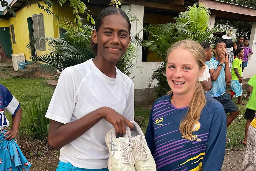 A Fijian netball player holds up sport shoes, next to Junee player Jorja Vergano
