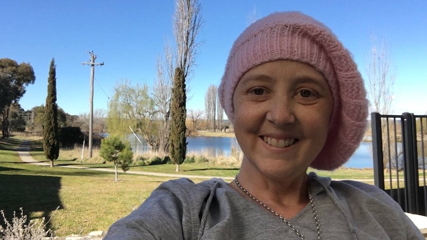 Close up shot of a woman wearing a beanie with a lake and trees in the background